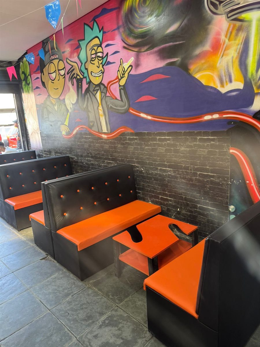 Bar com sofás booth preto e laranja e mesa narguilé, com grafite na parede